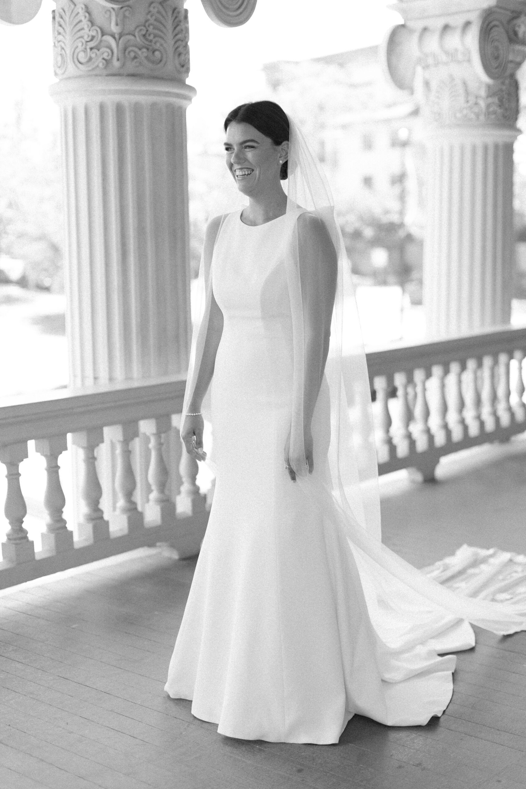 black and white photo of a bride waiting to see her bridesmaids for a first look. standing on the balcony of hotel ella in austin photograph taken by wedding photographer in austin alyssa nikole